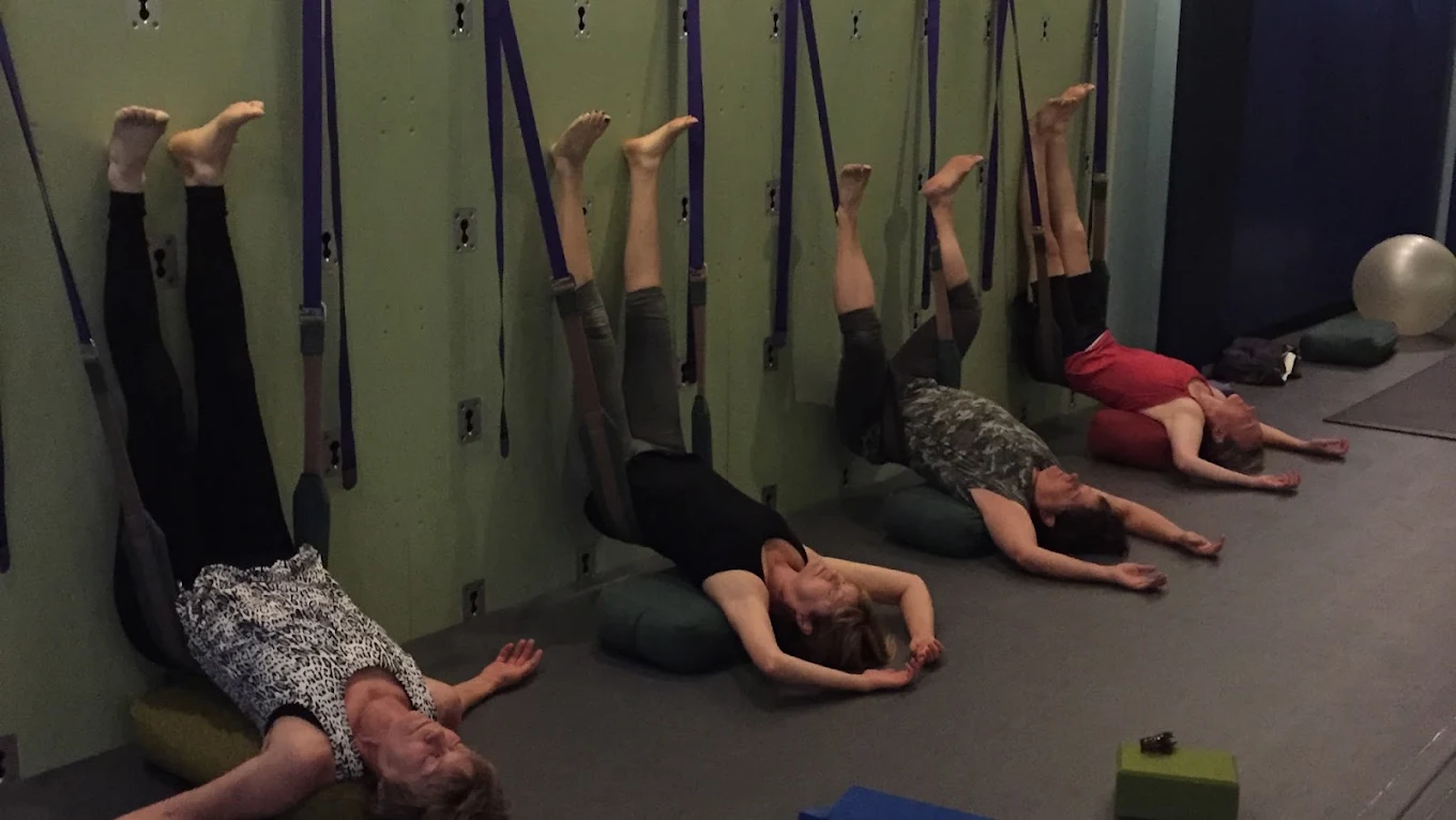Students resting with legs supported up the Yoga Wall on straps and bolsters during a Stretch and Strengthen class at Palm Yoga in Tampa